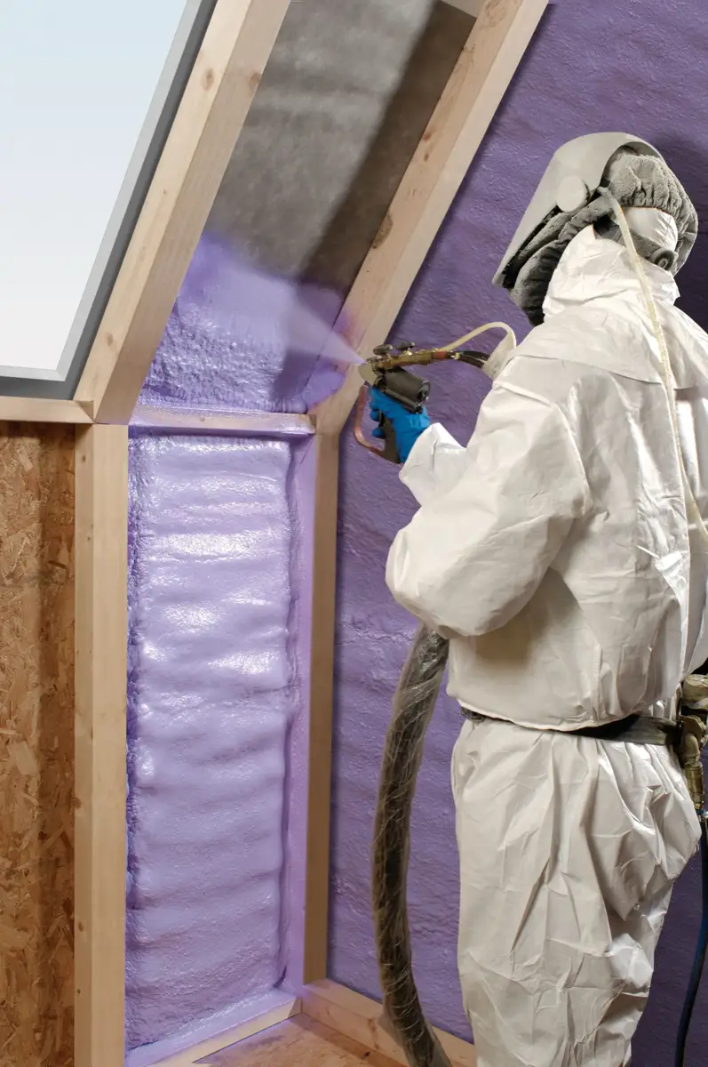 Applying spray foam across roof framing and walls